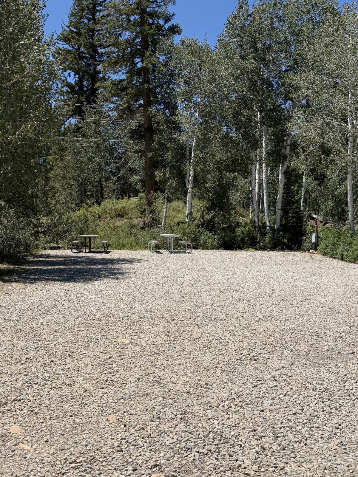 Gravel RV space with picnic tables surrounded by trees